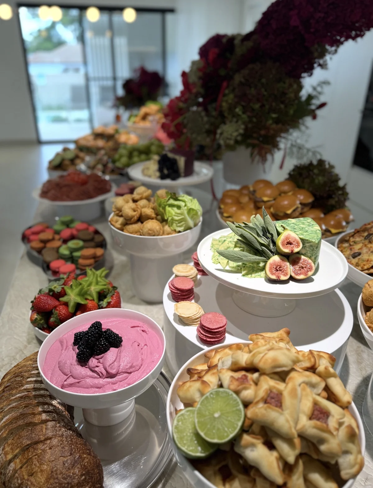 A grazing table with pastries, dips, artisan cheese, fruit and sliders